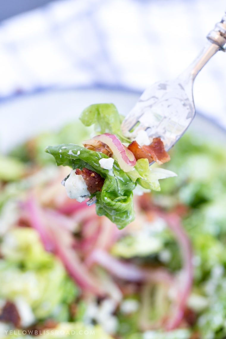 A fork with lettuce, ranch dressing, onions and bacon.