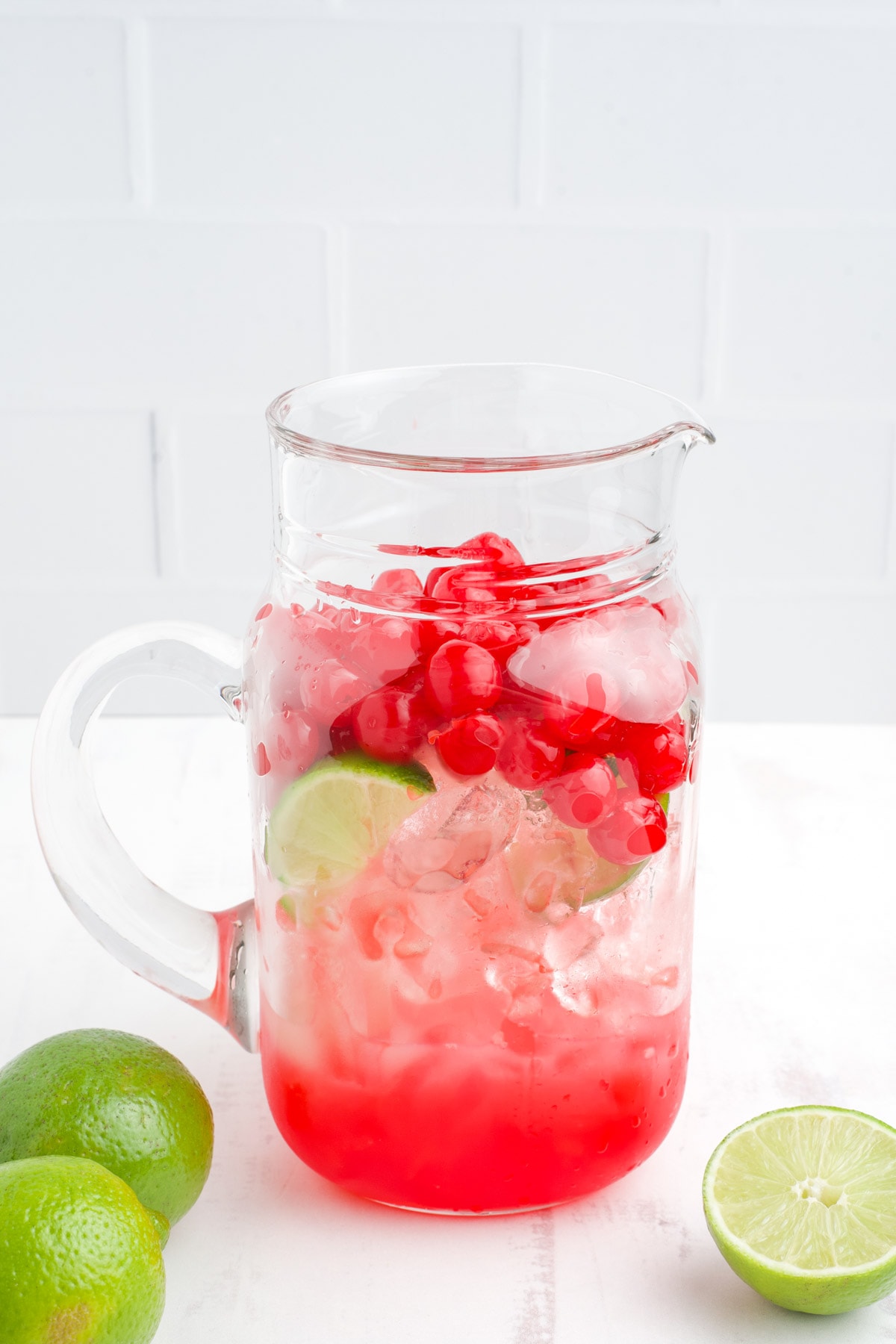 Ice, limes and cherries in a large pitcher. 