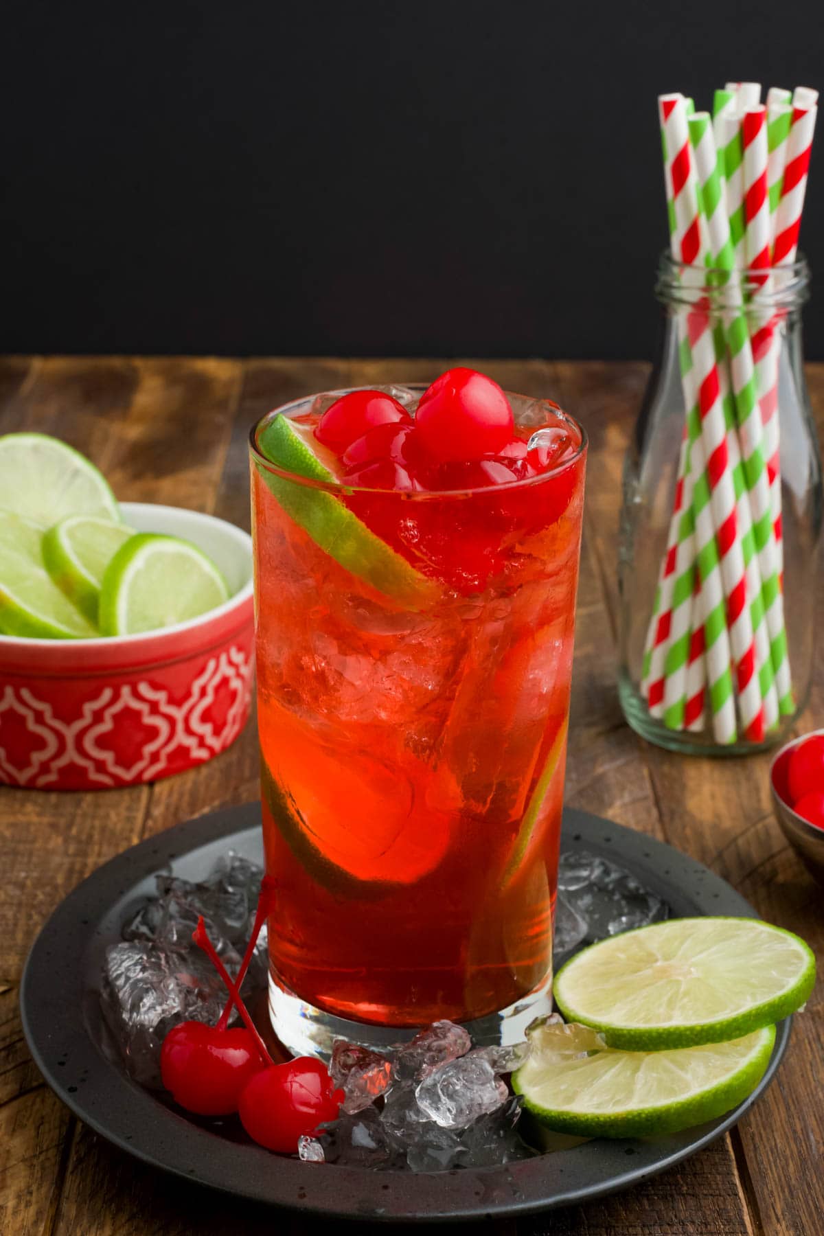 Red beverage with limes and cherries in a tall glass.