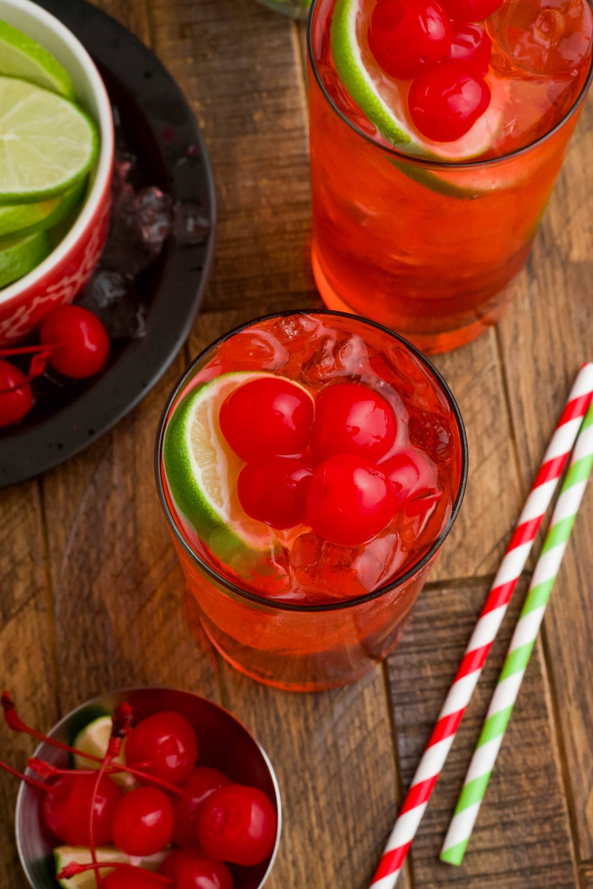 Red beverage with cherries and limes in a tall glass.