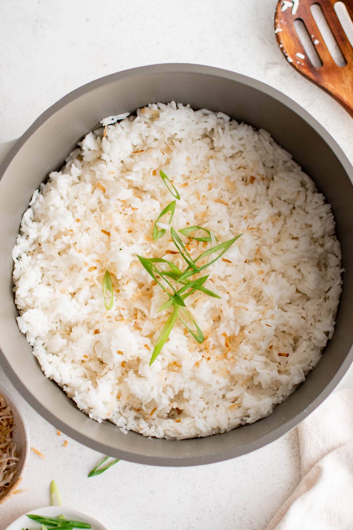 Saucepan with homemade coconut rice topped with toasted coconut and sliced green onions.