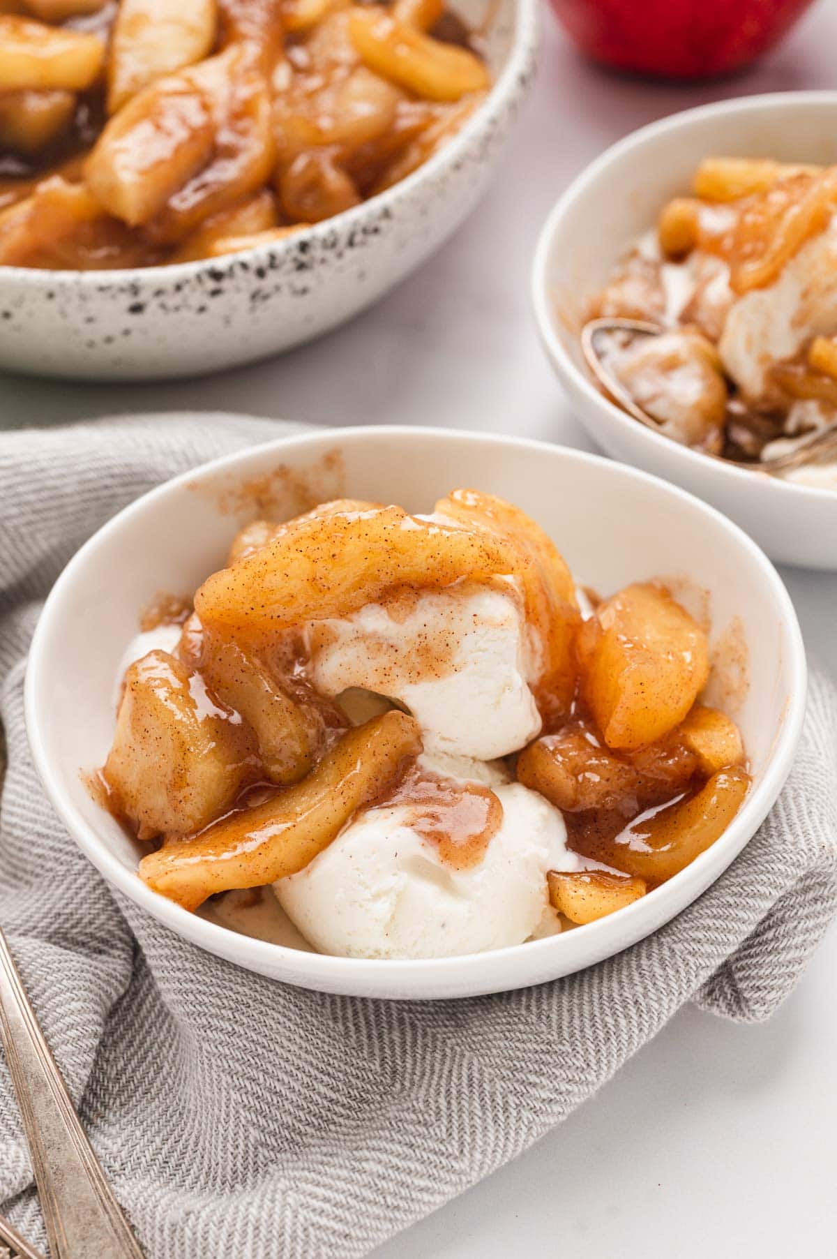 Caramelized apple slices in a white bowl with vanilla ice cream. 