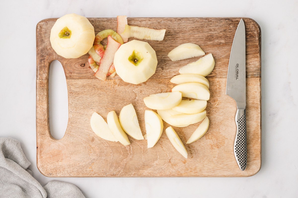 Peeled and sliced apples on a cutting board with a knife.
