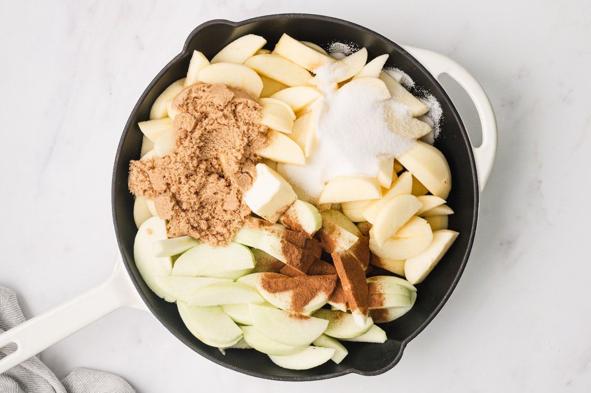 Sliced apples in a large skillet with brown sugar and cinnamon.