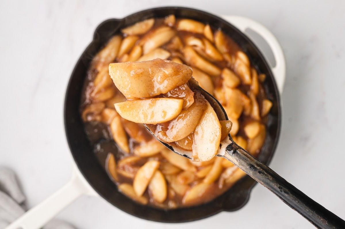 Sliced apples in a syrupy sauce with a large spoon over a skillet.