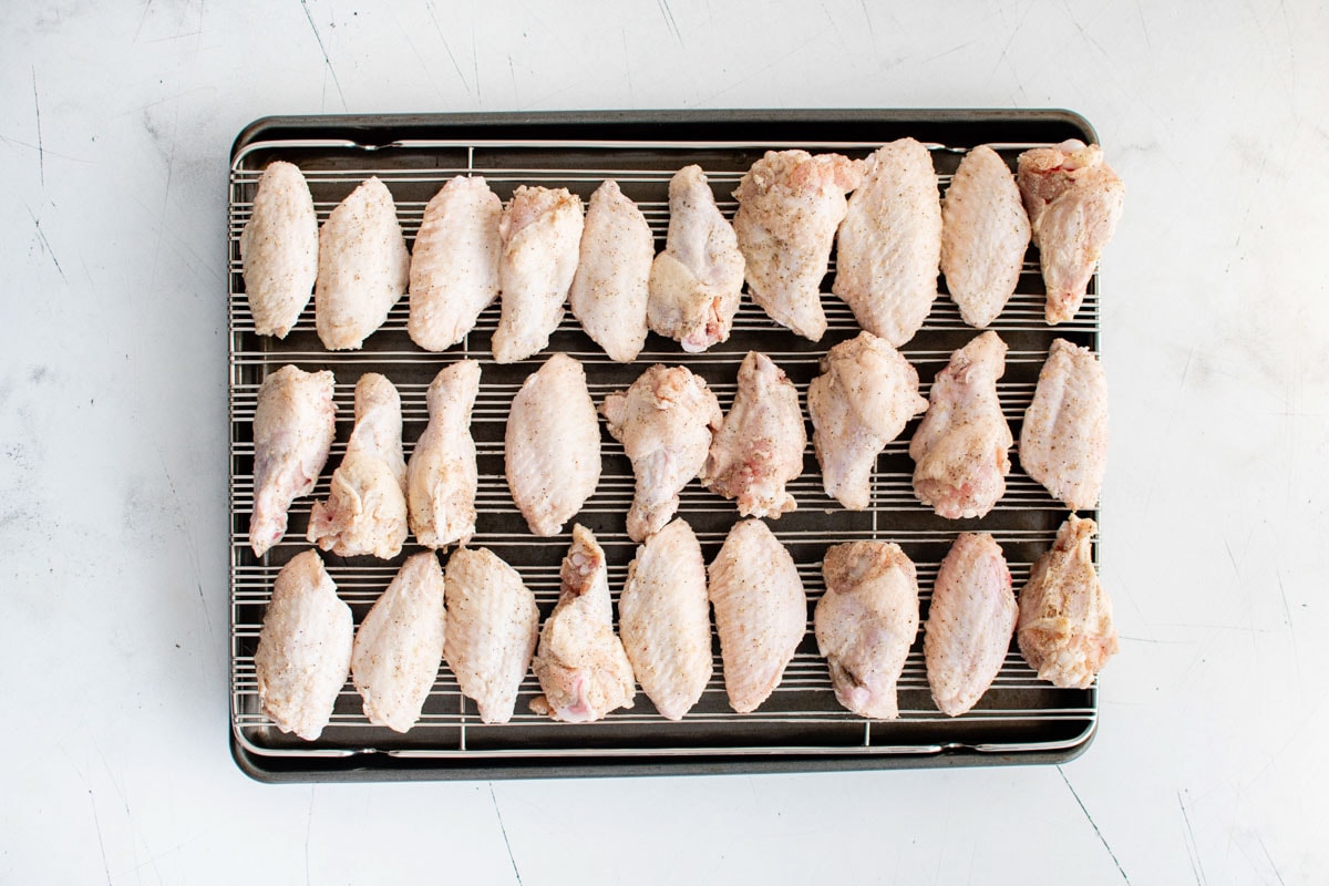 Uncooked chicken wings on a baking rack.