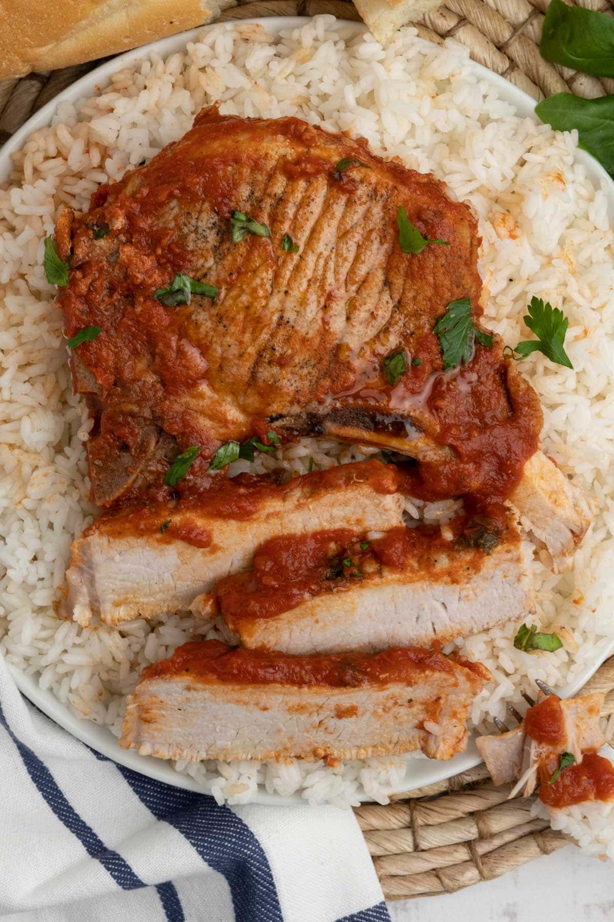 Pork chop with tomato sauce, served over white rice on a white plate.