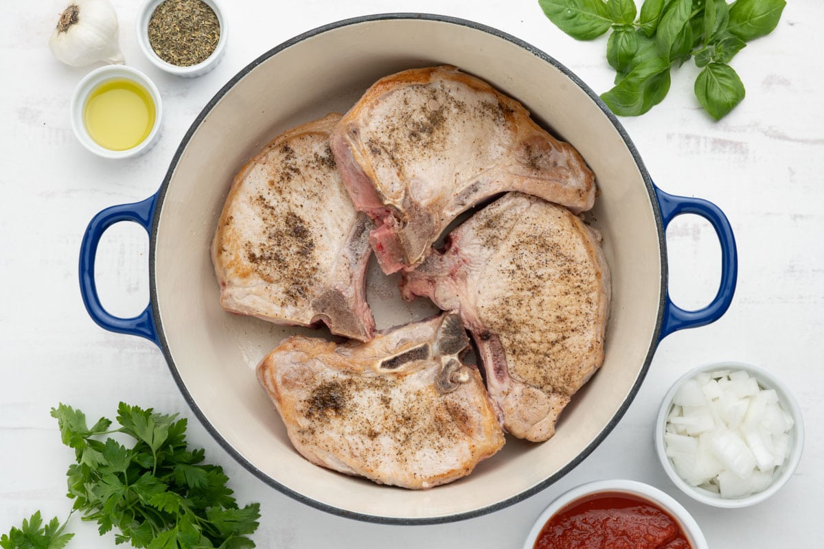 Seared pork chops seasoned with salt and pepper in a large dutch oven.