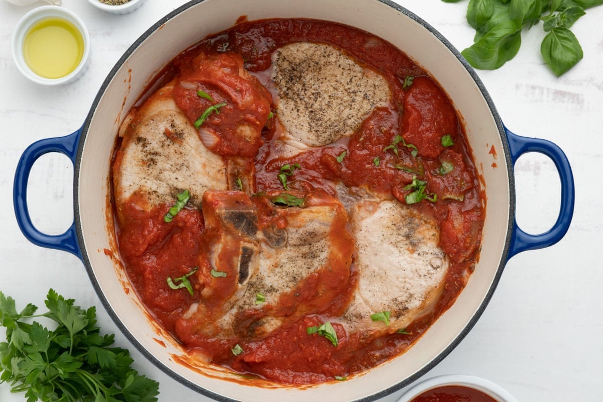 Pork chops partially covered in tomato sauce in a dutch oven.