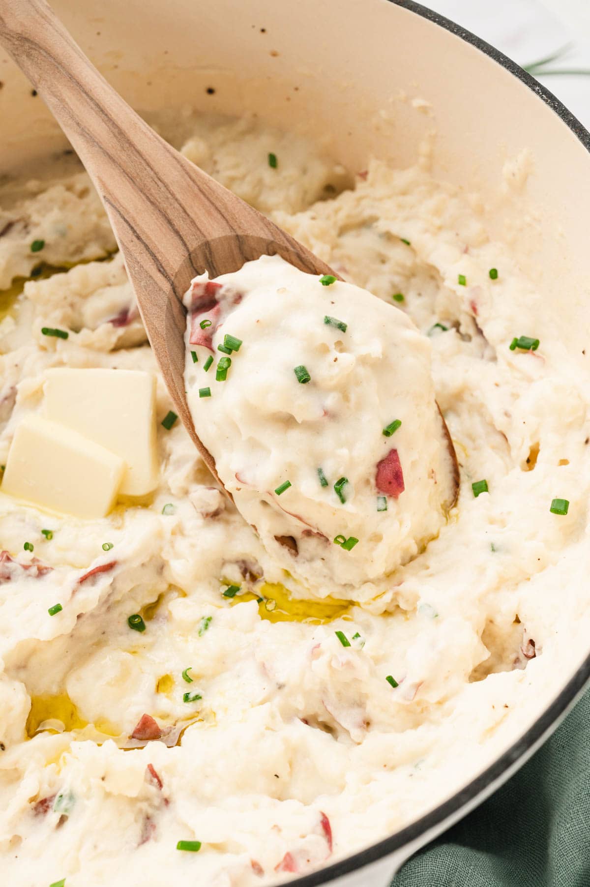 Pot of mashed potatoes with red skins and a wooden spoon.