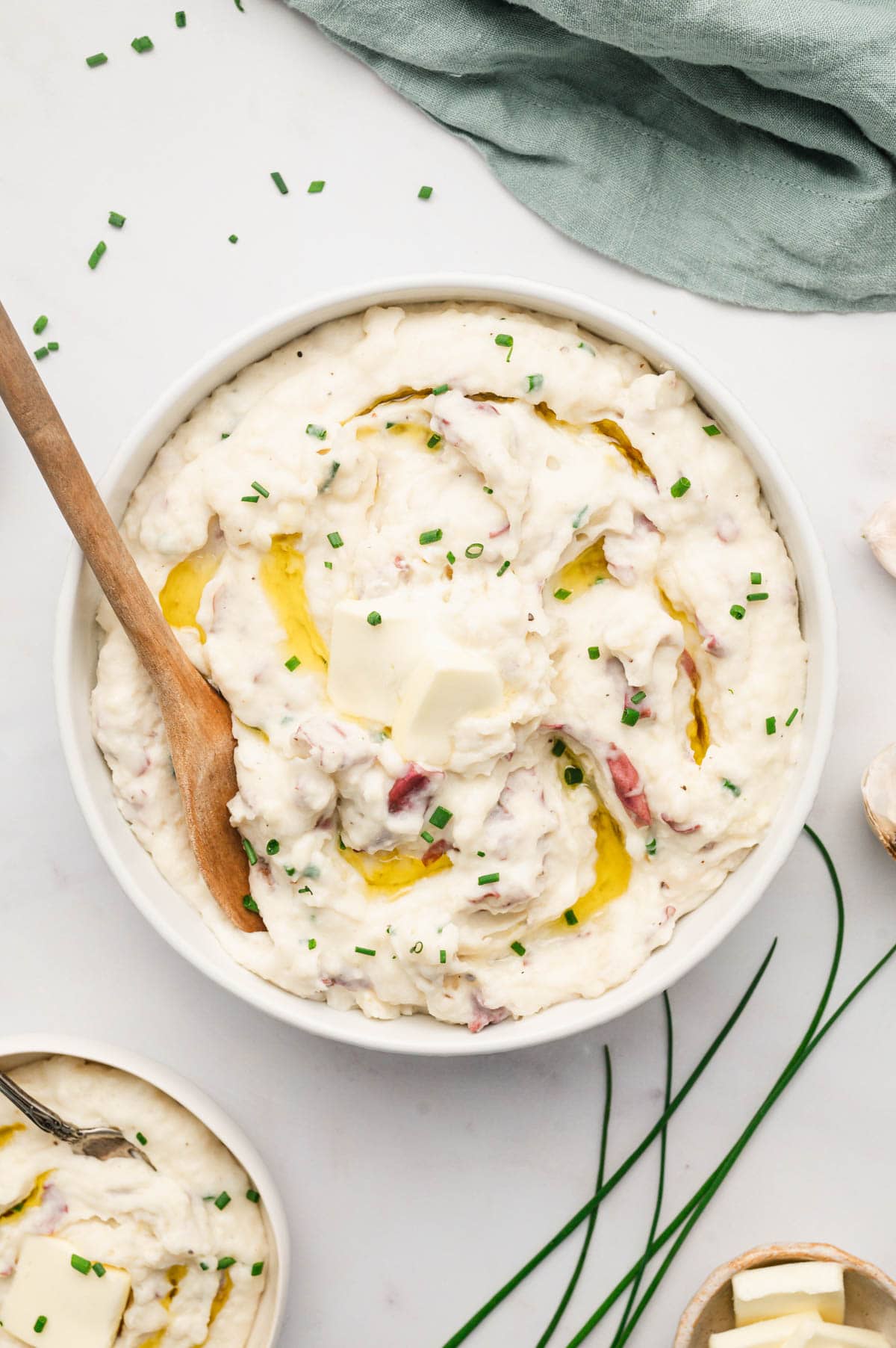 Large white serving bowl filled with red skinned mashed potatoes and a wooden spoon.