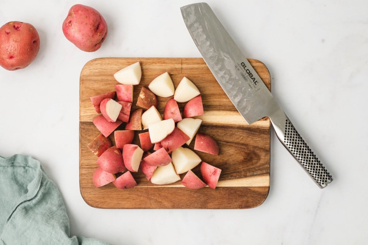 Cubes of red skinned potatoes on a cutting board and a silver knife.