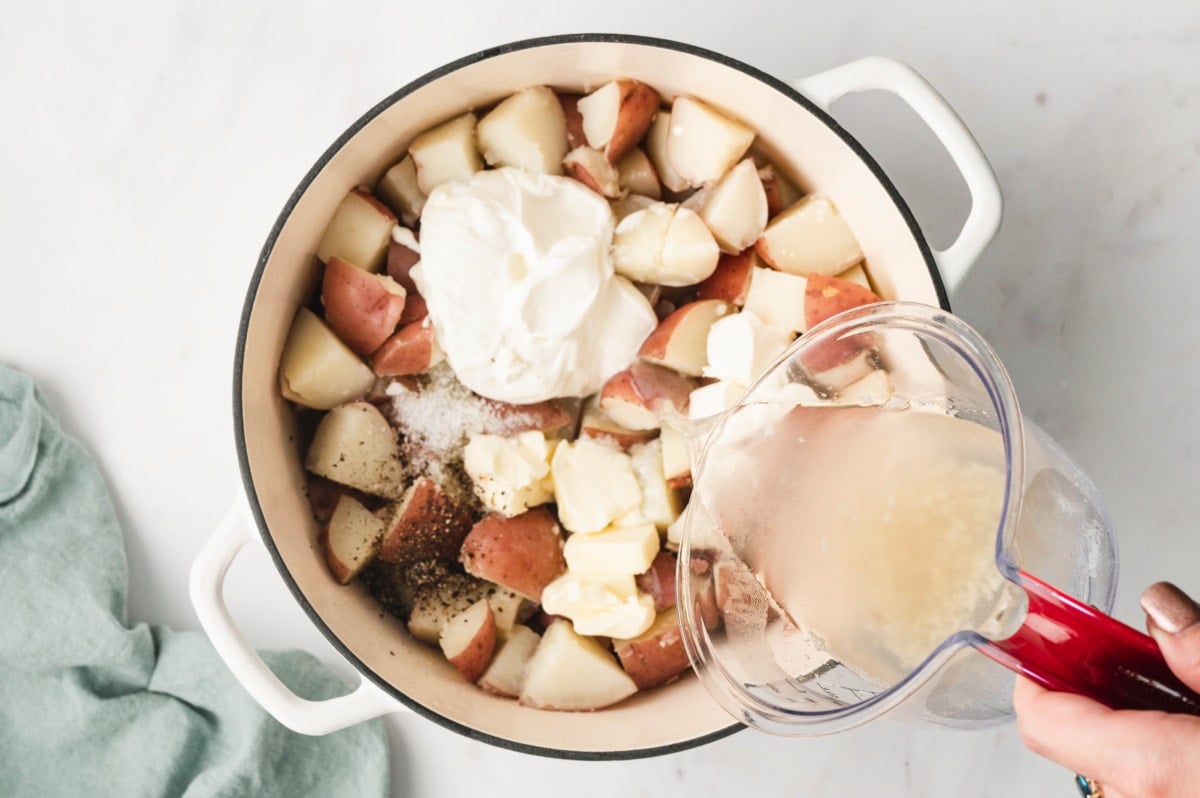 Cubed potatoes and sour cream in a large pot. Pouring liquid from a measuing cup.