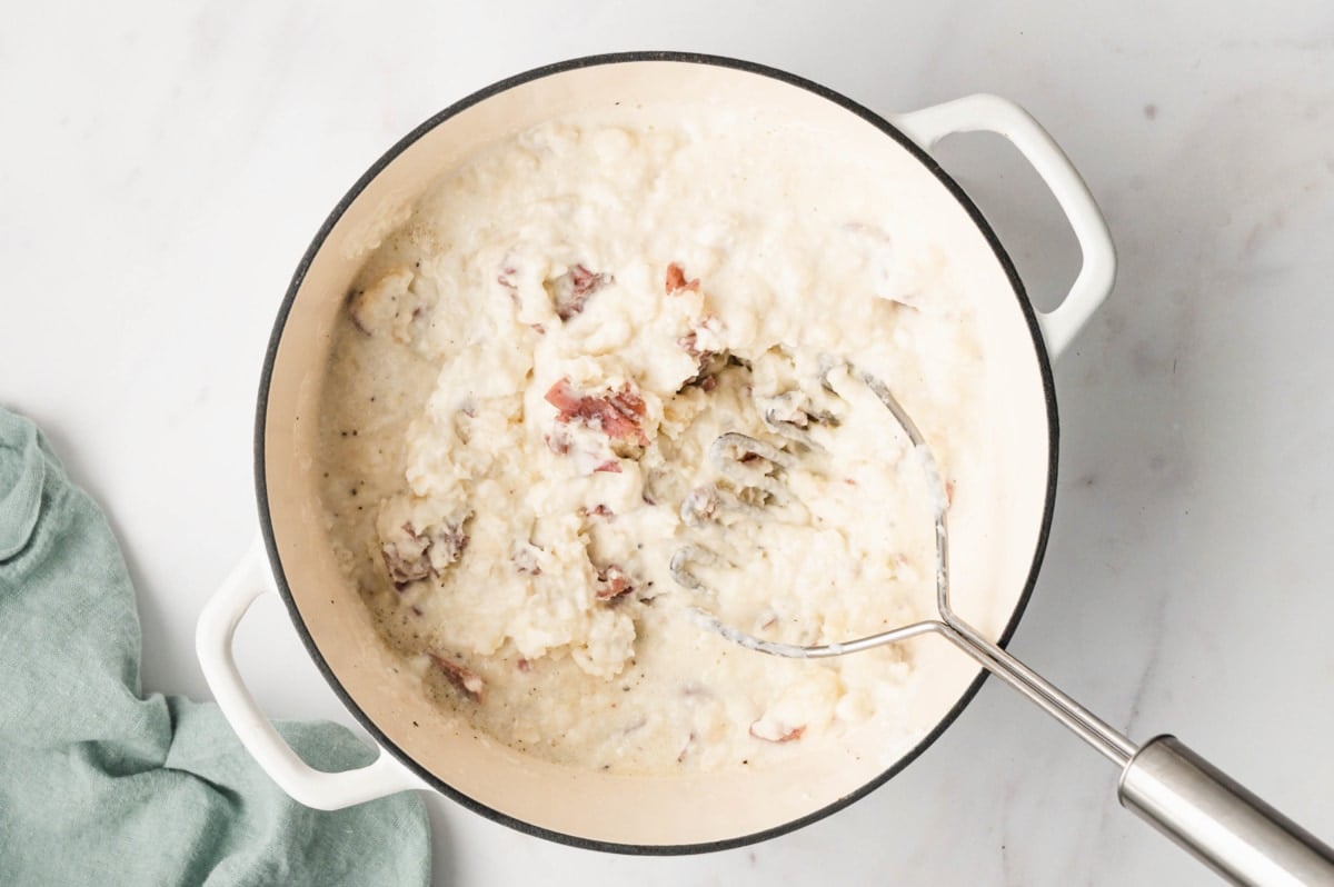 Mashed potatoes in a large pot with a potato masher.