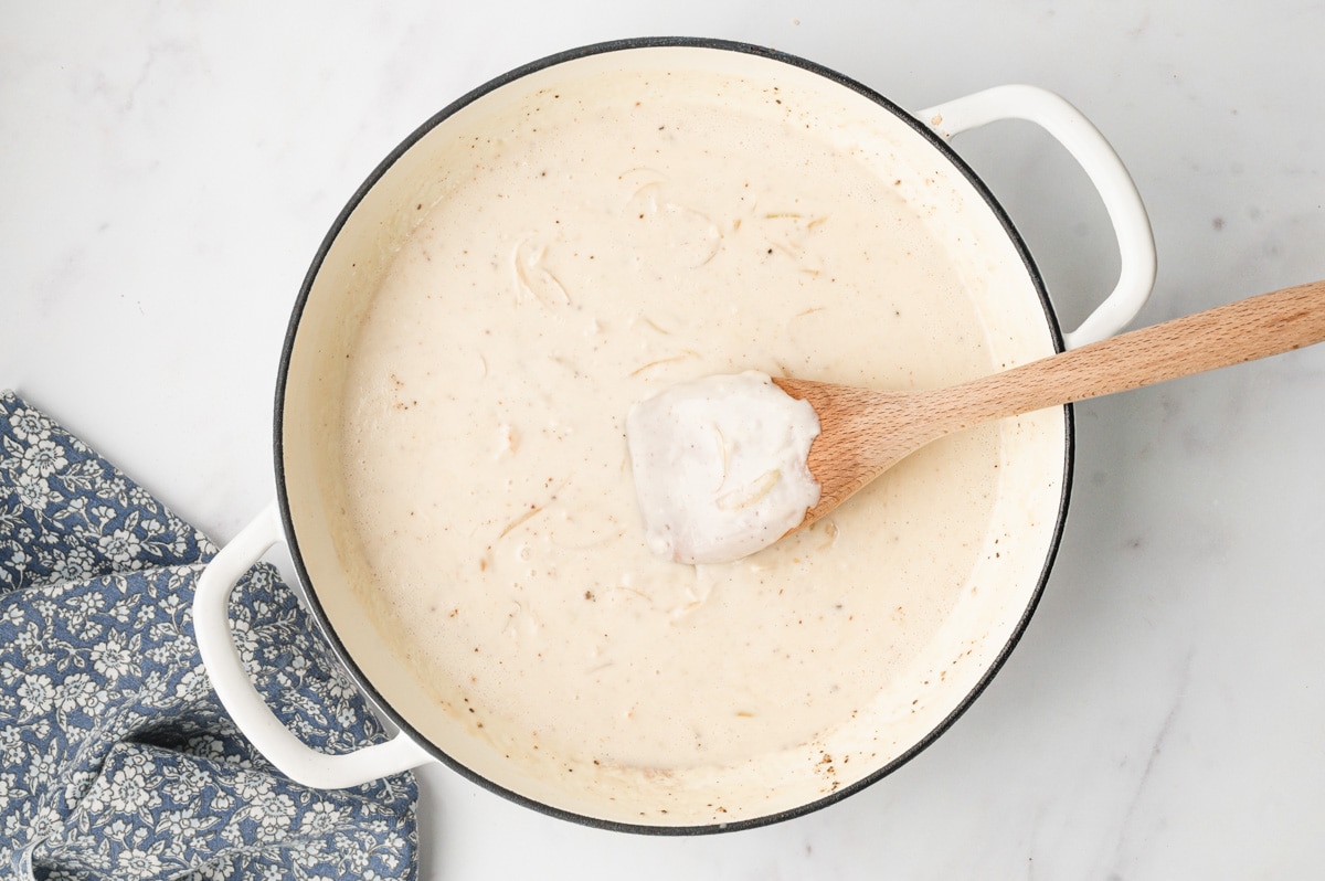 Light colored gravy in a skillet with a wooden spoon.