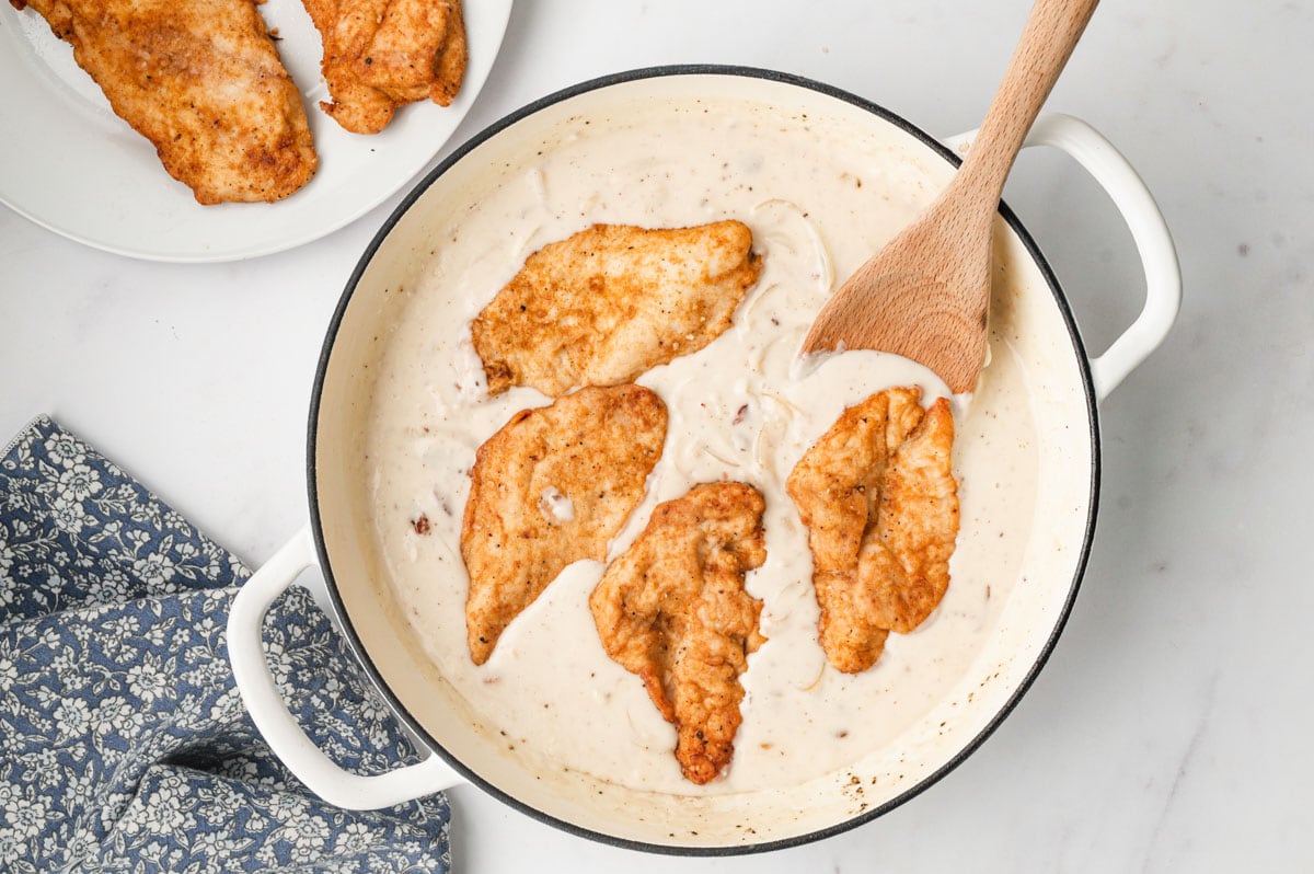 Pan fried chicken breasts in a skillet with gravy.