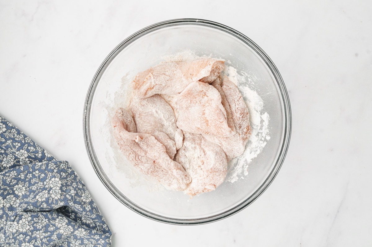 Thin chicken breasts in a bowl coated with flour.