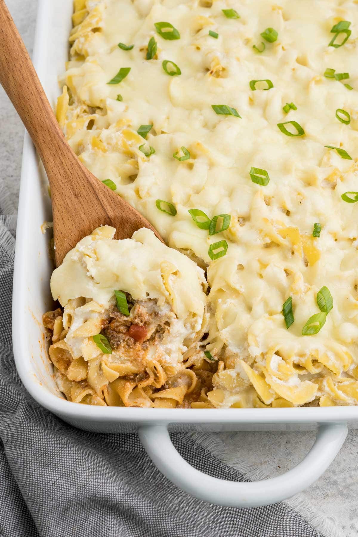 Pasta, cheese and sauce in a casserole with a wooden spoon.