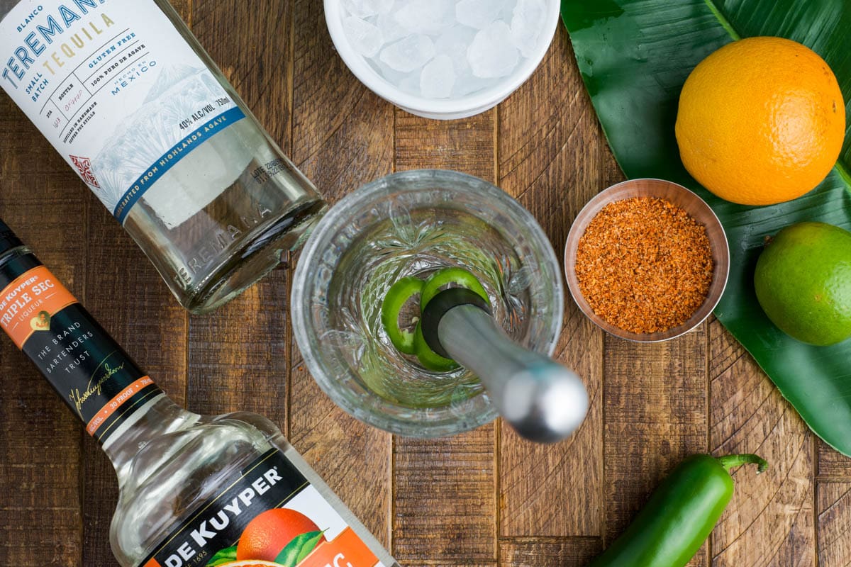 Muddling jalapeno slices in a glass.