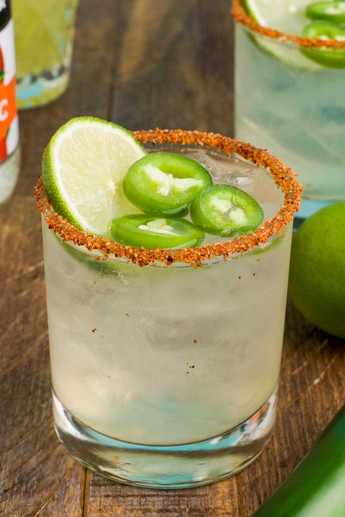 Margarita in a glass with jalapeno slices, lime slices and tajin on the rim.