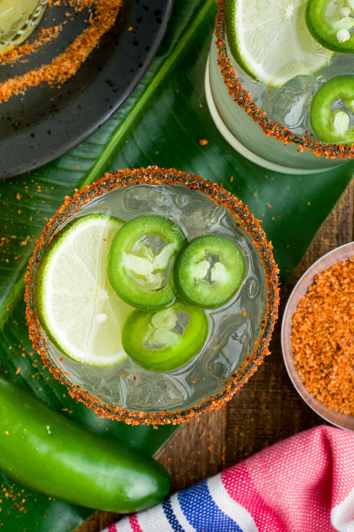 Overhead view of margaritas in glasses with slices of jalapeno and lime.