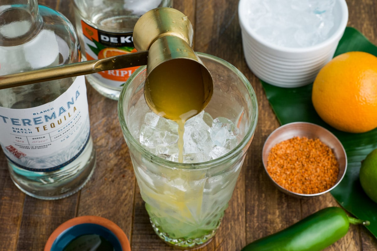 Using a jigger to pour ingredients into a cocktail shaker.