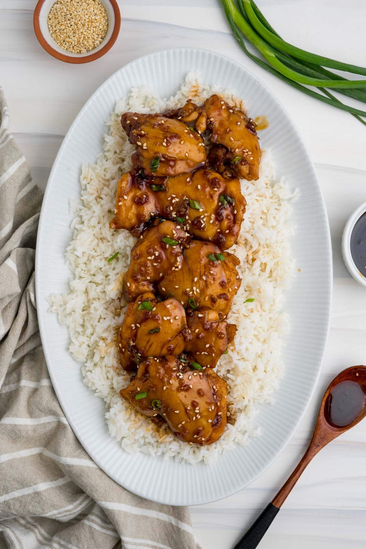 Sticky chicken thighs on a bed of white rice on a large white platter.