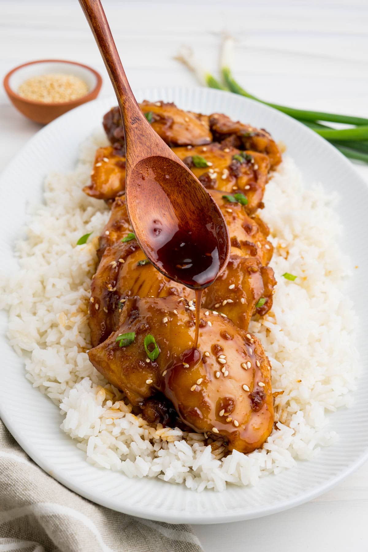 Sticked sauce coated chicken thighs on a bed of white rice with a wood spoon pouring sauce over them.