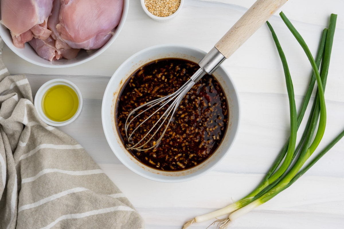 A dark sauce in a small white bowl with a whisk.