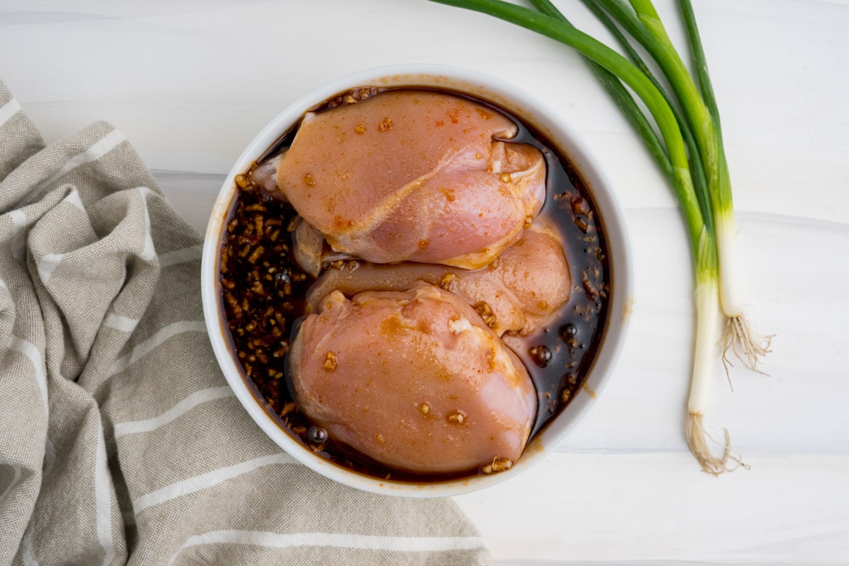 Uncooked chicken thighs in a white bowl with a dark liquid.