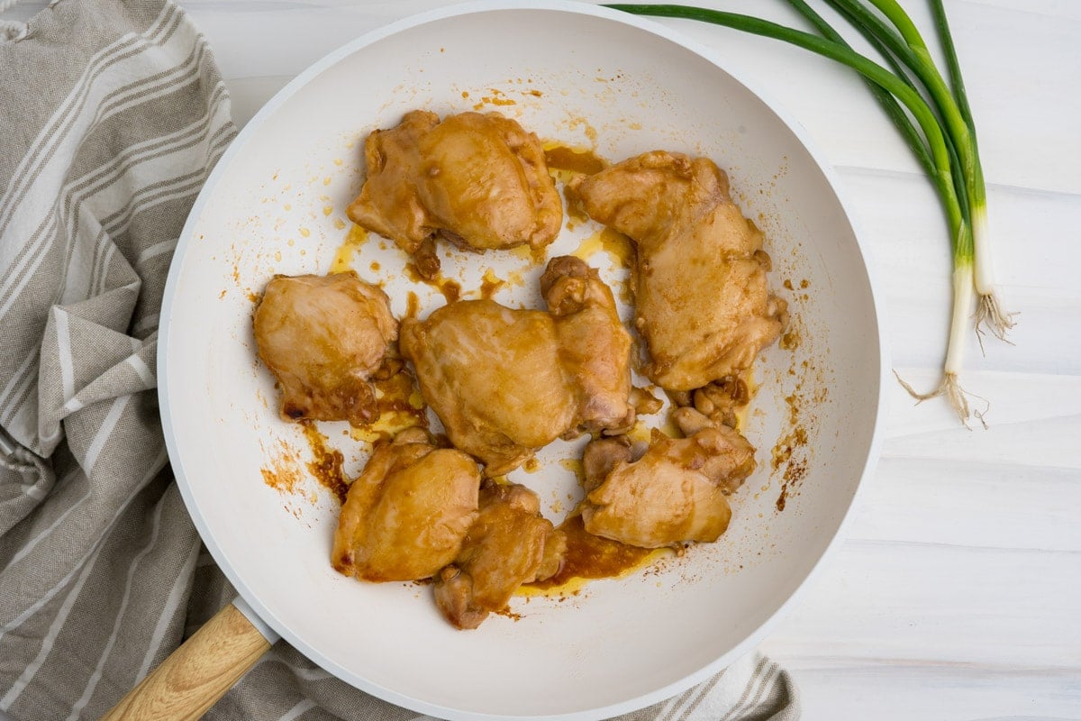 Cooked chicken thighs in a white skillet.