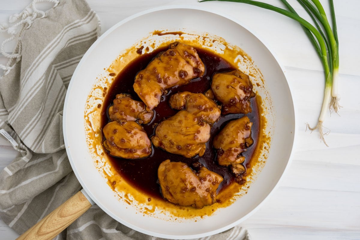 Cooked chicken thighs in a dark brown sauce in a white skillet.