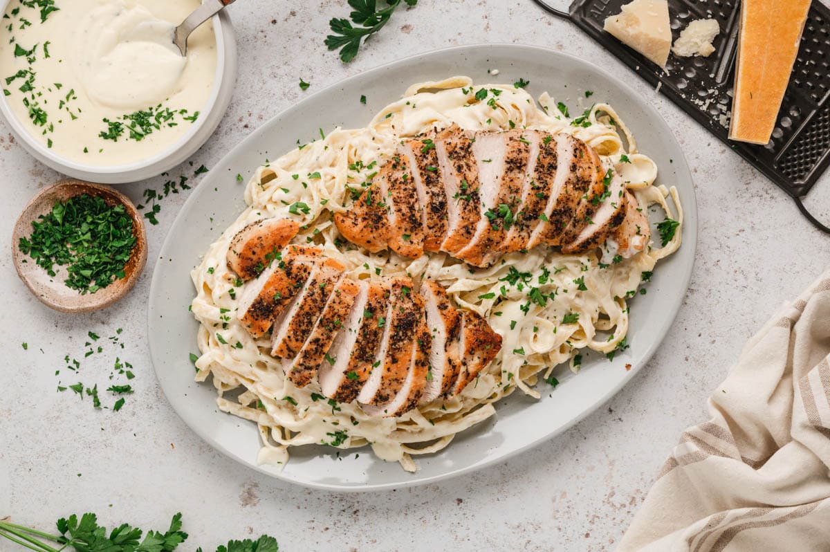 Large serving platter with fettucine and alfredo sauce and sliced chicken.