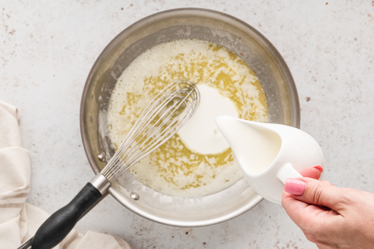Cream being poured into a skillet with melted butter.