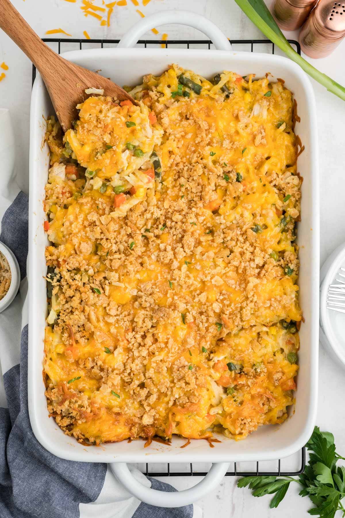 Casserole dish with chicken potato casserole with a cheese and cracker topping; a wooden spoon sits in the dish.