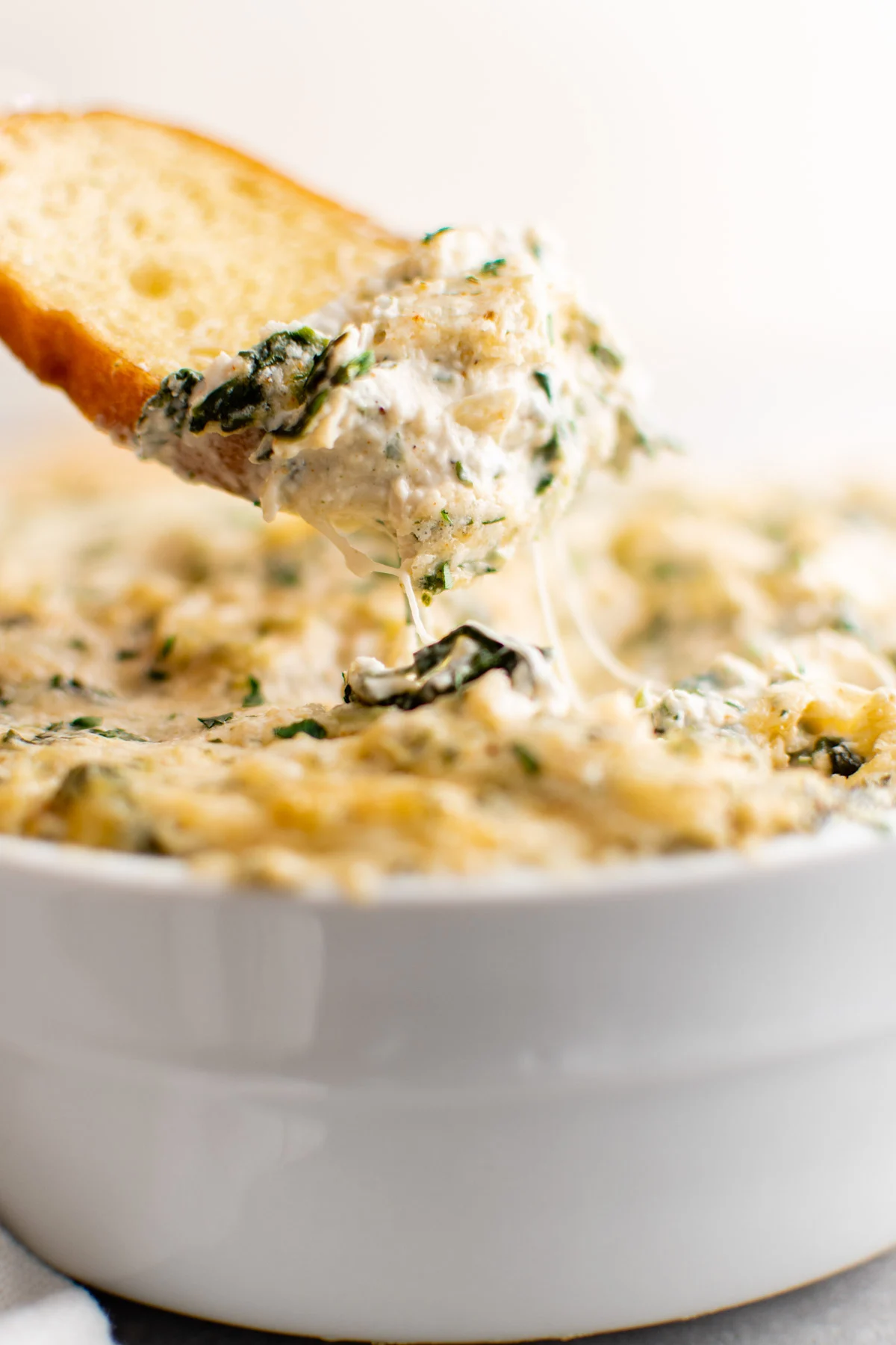 Crostini dipped in crab artichoke dip in a bowl.