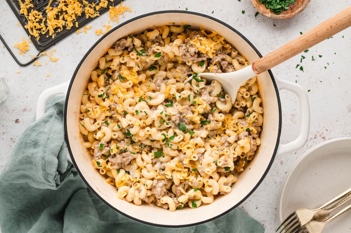 Hamburger mac and cheese in a large dutch oven with a wooden spoon.