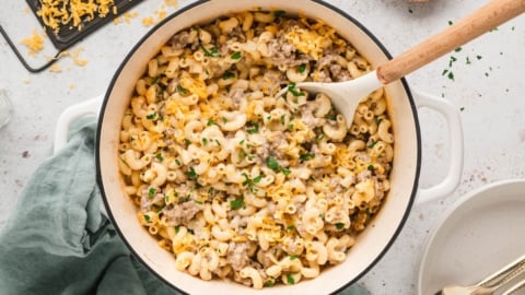Hamburger mac and cheese in a large dutch oven iwth a wooden spoon.