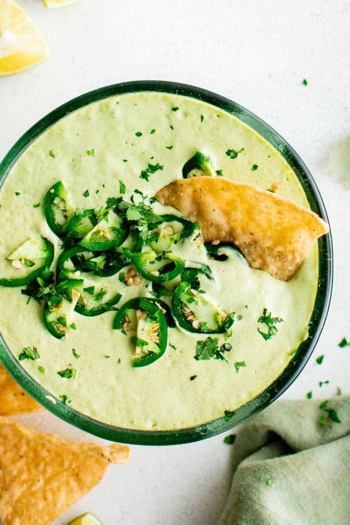 Creamy green dip with sliced jalapenos and a tortilla chip.