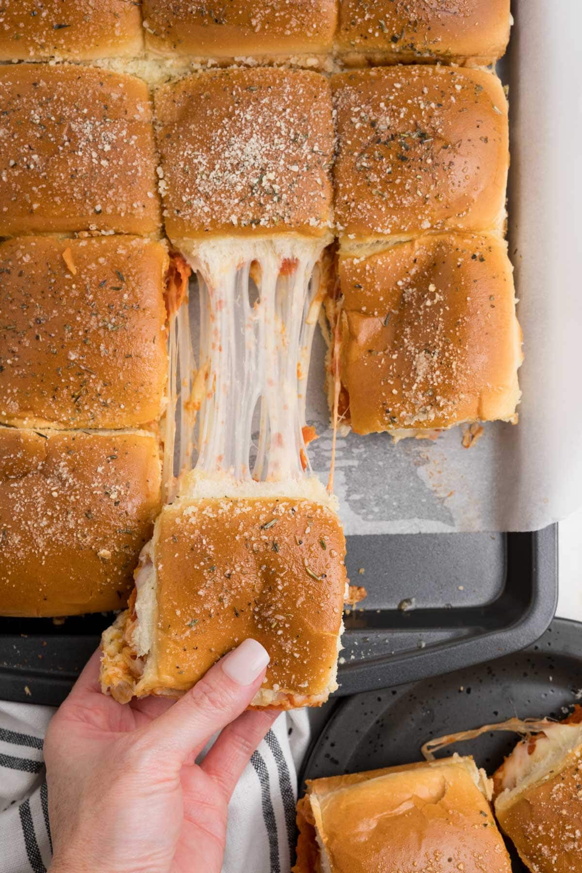 Sliders with cheese stretching and a hand pulling one slider.