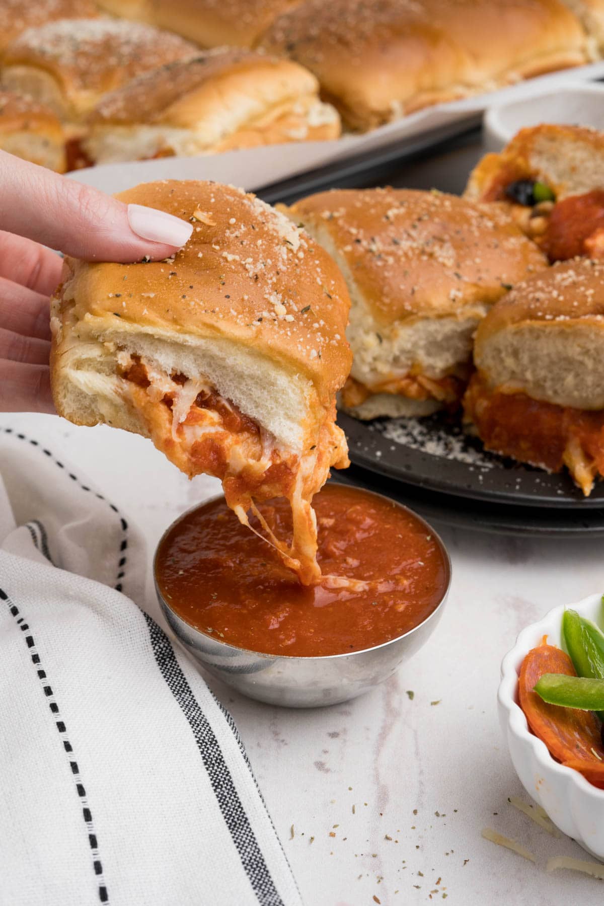 A hand holding one slider and dipping it in pizza sauce.