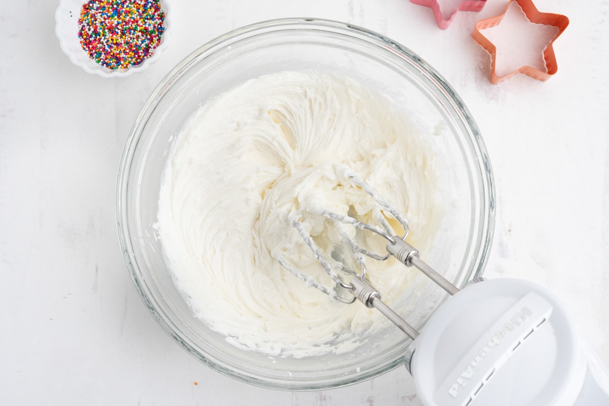 White frosting in a glass bowl with a hand mixer.