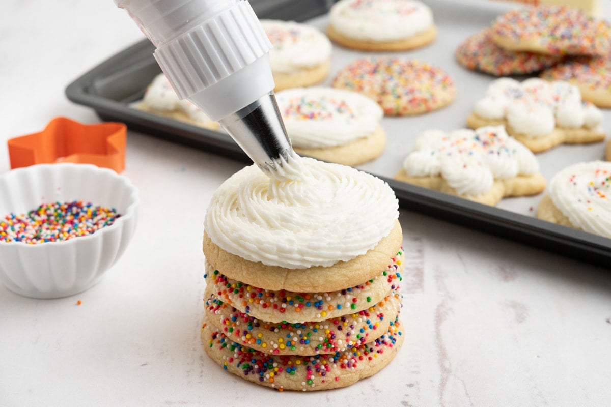 Stack of sugar cookies, white frosting piping out onto the top one.