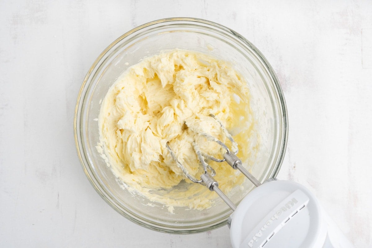 Light yellow butter mixture in a bowl with a hand mixer.