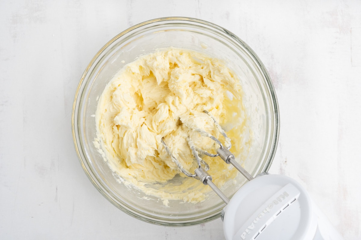 Light yellow butter mixture in a bowl with a hand mixer.