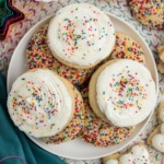 Sugar cookies on a plate with white frosting and sprinkles.