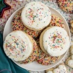 Sugar cookies on a plate with white frosting and sprinkles.