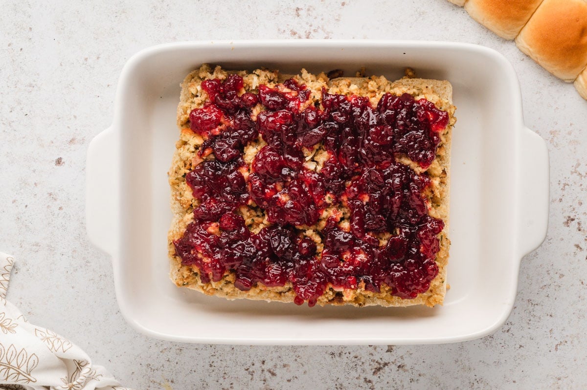 A layer of cranberry sauce over stuffing on a slab of rolls.