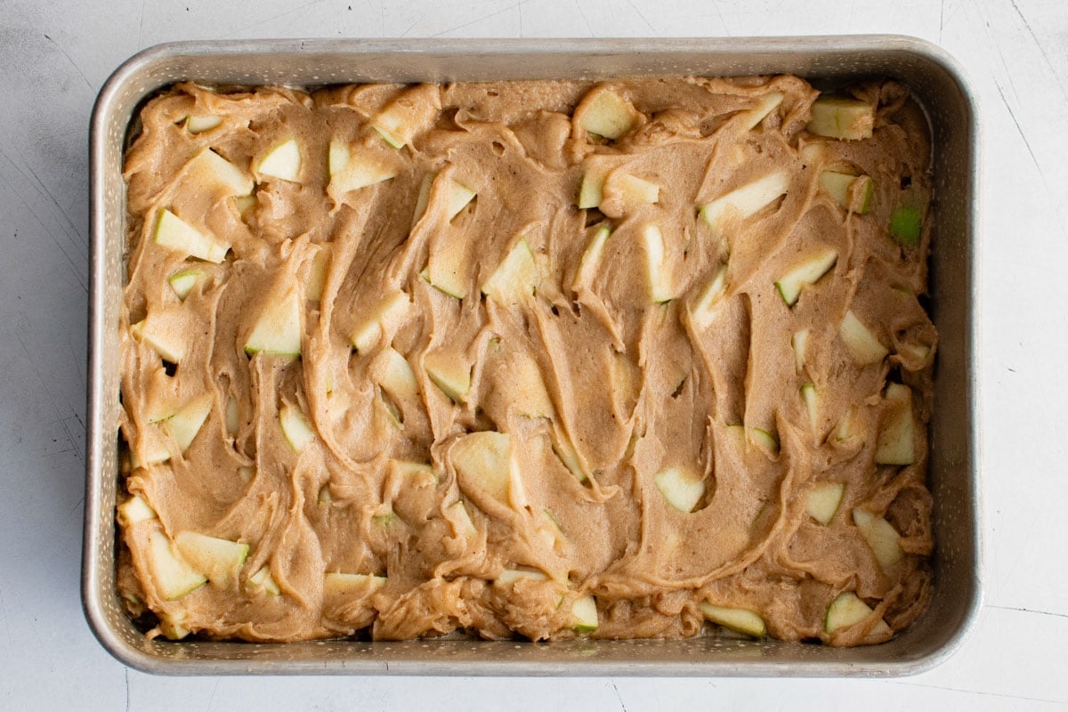 Cake batter with apples in a baking pan.