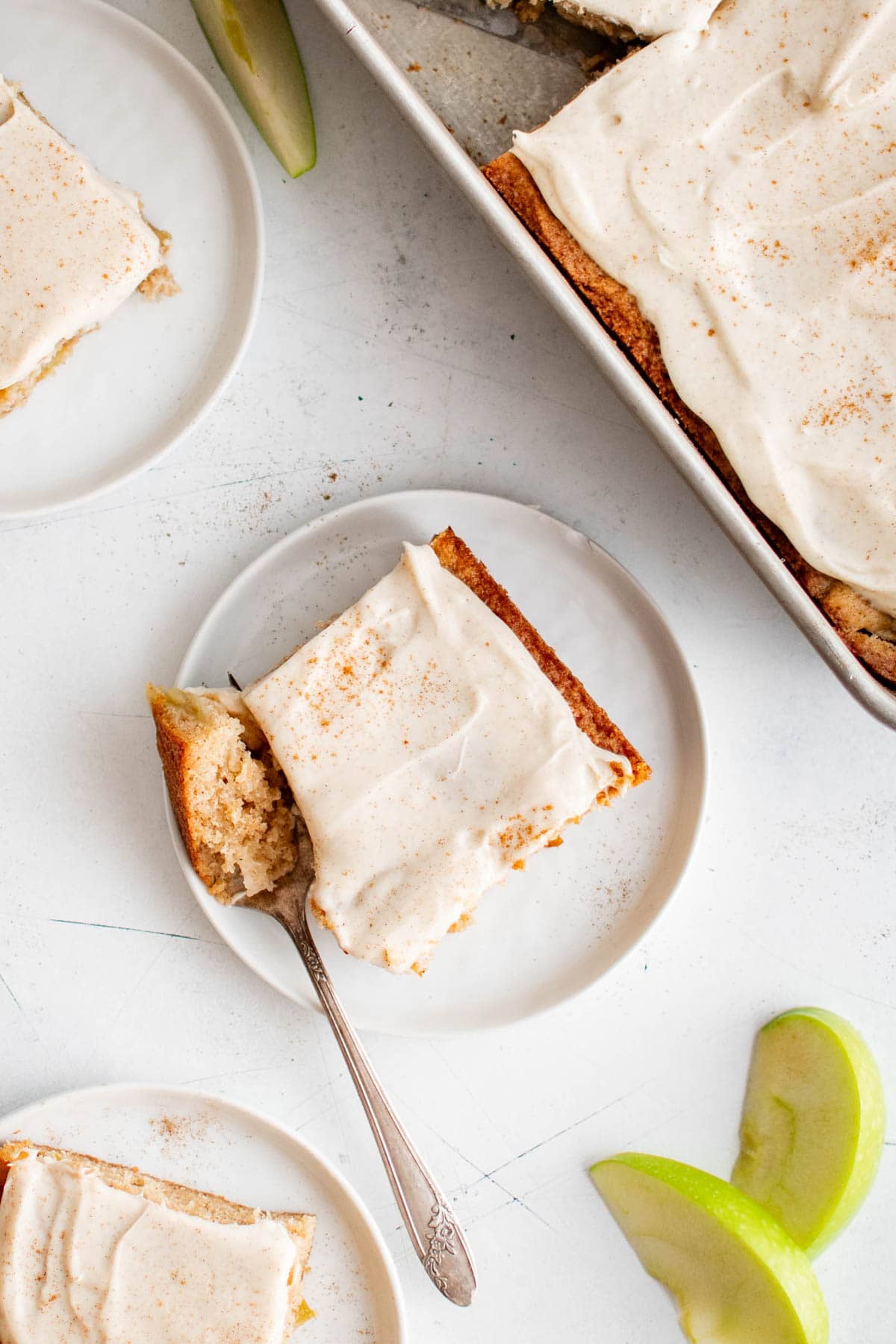 Slice of apple cake with frosting on a small white plate with a fork.